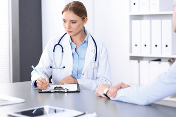 Doctor and patient in clinic. Beautiful blonde physician consulting business man about his health. Medicine concept