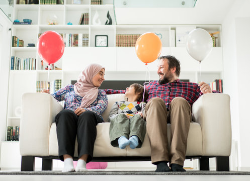 Muslim family with balloons sitting on sofa in living roome at home