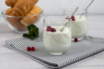Homemade yogurt in two glasses on a light wooden background. Decorated with mint and cranberry berries. Healthy diet food. Vegetarian food.