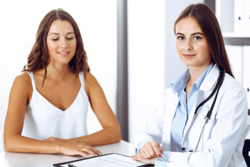 Doctor and happy patient talking while sitting at the desk. The physician or therapist discussing healthy lifestyle. Health care, medicine and patient service concept