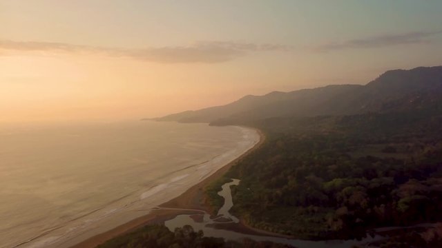 Aerial Drone view of the sunset at beach / coastline in Costa Rica with rain forest, palm trees and mountains at the Marino Ballena National Park in Uvita