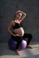 Fototapeta na wymiar Portrait of pretty pregnant woman exercises with fitball in the gym. Working out and fitness, pregnancy concept