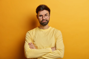 Serious man frowns face, stands impatient, keeps arms folded, waits for explanations, being...