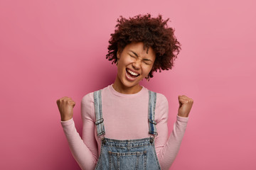 Triumphing upbeat woman makes fist bump, exclaims hooray, celebrates winning victory, rejoices team...