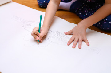 kids hobby. a little six year old child girl draws with a pencil on paper sitting on the floor at home. the concept of home exercises during the coronavirus covid-19 quarantine