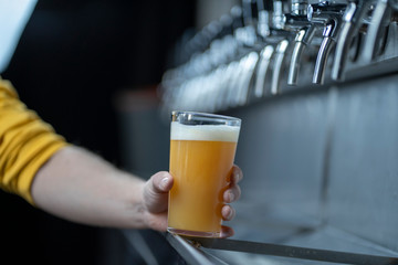 Hand holding a pint of wheat beer on stainless steel taps backgorund