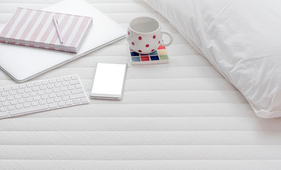 work from home concept with white keyboard, laptop, smartphone and mug on the bed.