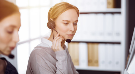 Businesswoman talking by headset in sunny office. Call center and diverse people group in business