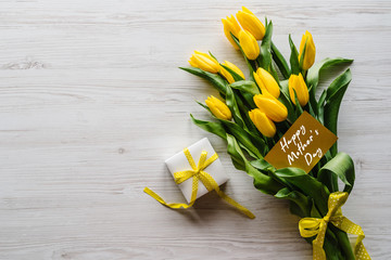 Happy mother's day text sign on craft postcard. Bouquet of tulips with gift box on white wooden background. Holiday greeting card for Mother's Day. Top view, flat lay. © Serhii