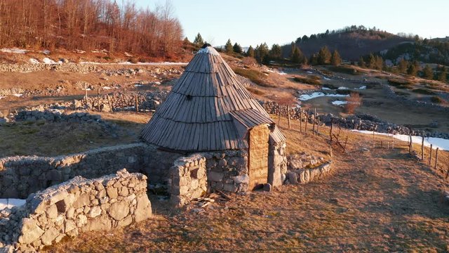Traditional round stone hut, with conical wooden roof, used by shepherds for livestock in mountainous pastures as summer grazing area. High mountains in Montenegro, Europe, in early spring.