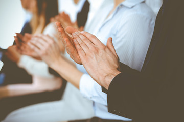 Obraz na płótnie Canvas Business people clapping and applause at meeting or conference, close-up of hands. Group of unknown businessmen and women in modern white office. Success teamwork or corporate coaching concept