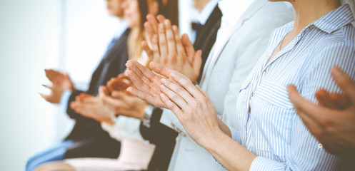 Obraz premium Business people clapping and applause at meeting or conference, close-up of hands. Group of unknown businessmen and women in modern white office. Success teamwork or corporate coaching concept