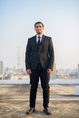 Full body shot of young Persian businessman in suit against view of the city