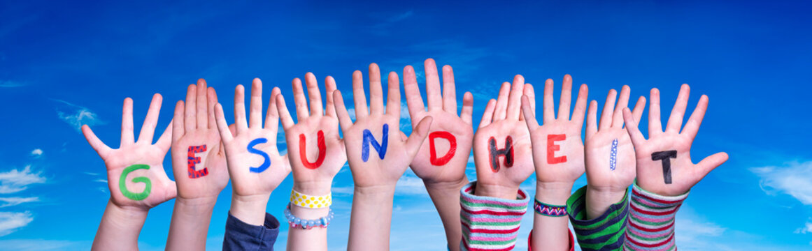Kids Hands Holding Colorful German Word Gesundheit Means Health. Blue Sky As Background