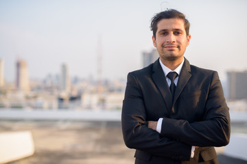 Young Persian businessman in suit with arms crossed against view of the city