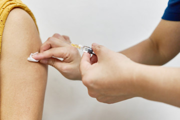 Hand of nurse holding hypodermic syringe and alcohol pad is injecting vaccine of flu with left shoulder of woman in brown blouse. Close up shoulder of woman. Healthcare and medical concept photography