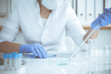 Professional female scientist in protective eyeglasses and mask making experiment with reagents in laboratory. Coronavirus pandemic stop. Medicine and research concept