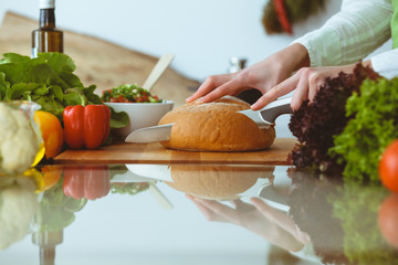 Unknown human hands cooking in kitchen. Woman slicing bread. Healthy meal, and vegetarian food concept