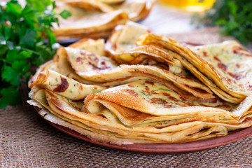 Traditional Russian thin pancakes or crepes with cheese, herbs on a plate on a light background