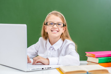 Smiling young gurl wearing eyeglasses uses laptop in a school