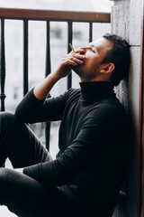 A man sits and smokes on the balcony. The guy smokes on the apartment balcony.
