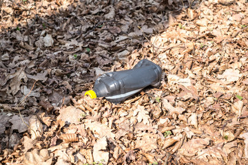 A dirty plastic and glass bottle left in the autumn forest. Plastic waste in the environment.