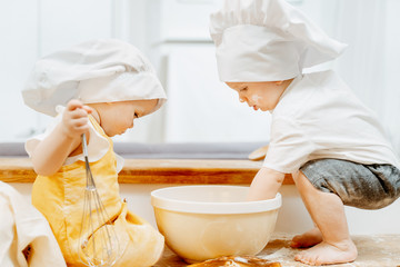 Side view of a cute little cook children in hats with interest prepare dough while sitting on a...