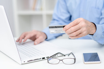 Hands of an elderly person hold credit card and use laptop. Online shopping