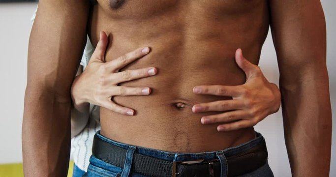 Close up of woman rubbing her hands across the abs of her boyfriend. Shirtless man in jeans being caressed by the hands of his lover. 4k slow motion handheld