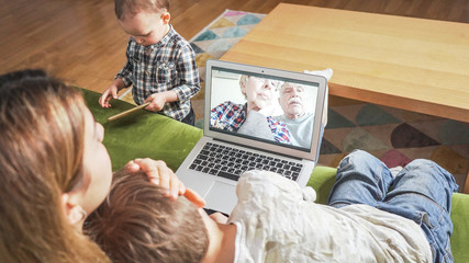 Young mom with two sons having a facetime video call with elderly grandparents. Family connecting with their parents on webcam. Modern technology connecting people of all ages concept.
