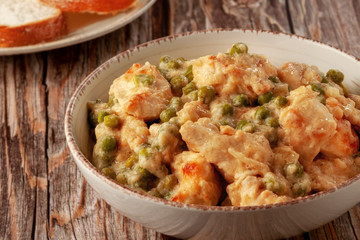 Chicken fillet with green peas stewed in a creamy sauce on a wooden table