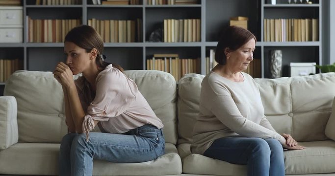Stressed unhappy grown up daughter and older mom sitting separately on couch in living room, ignoring each other after misunderstanding or quarrel, relationship problems, generations gap concept.