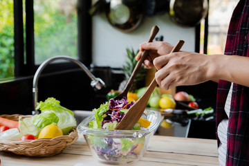 Man mixing fresh vegetables in a bowl while standing in the kitchen.making salad.Homemade