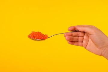 Spoon with red caviar on a yellow background
