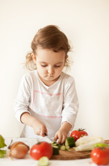 Cute curly girl prepares vegetables for salad in home kitchen. Healthy eating.