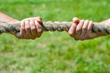 Two men's hands pull the rope each in his own direction. The concept of dispute, conflict and force