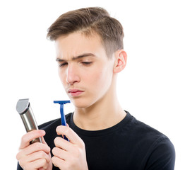 Teenager holds a razor and an electric razor while looking at the camera. Teenager chooses which...