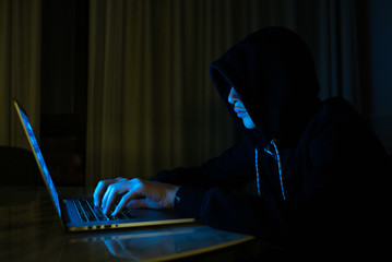 Hacker is  hacking into the computer network. Young boy in a dark room with laptop.  Hacker with a...