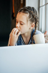 Girl student study online with video call teacher, Happy young girl listen lecture watch at laptop at home and drink tea and eat cookies. Covid-19 coronavirus.