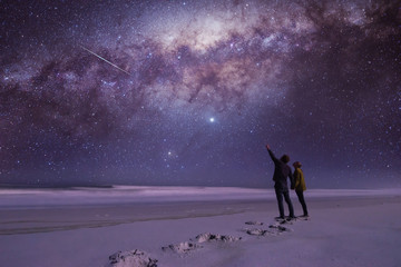 Couple holding hands looking and pointing in amazement at a shooting star while standing on a...