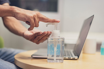 Close up of hands using antiseptic gel, alcohol gel to disinfect hands over a work desk in at home. Preventive measures during the period of epidemic and social distancing. Covid 19, Coronavirus