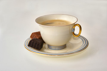Coffee cup and pralines on a white background decorative art style with golden handle set of cup and saucer with two choclate pralines