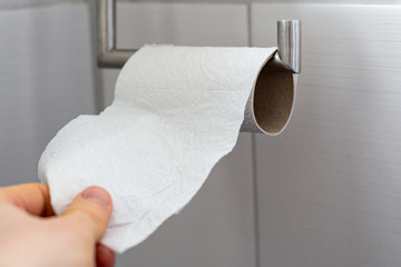 Man grabs toilet paper from an almost empty roll close up
