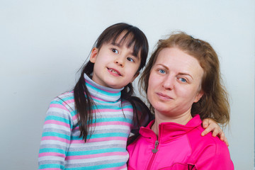 a mother with blond hair and her daughter are smiling and hugging. posing for the camera