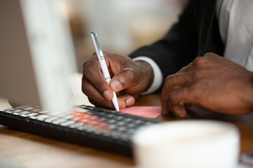 Making notes, close up. African-american entrepreneur, businessman working concentrated in office. Looks serios and busy, wearing classic suit. Concept of work, finance, business, success, leadership.