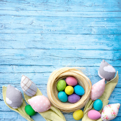 Rustic easter background for advertising or banner, Instagram post. Patchwork tulips from textile and multi-colored Easter eggs on a background of blue wooden boards.