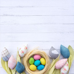 Easter nest with colorful eggs surrounded by fabric tulips flowers on a background of white wooden...