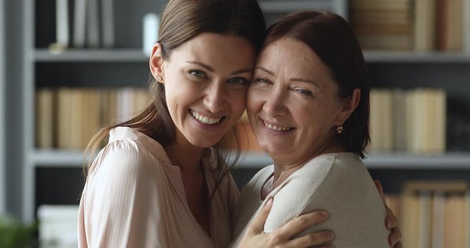Happy young woman embracing smiling middle aged woman, enjoying closeness sweet moment, posing for photo. Headshot portrait of bonding devoted two female generations family looking at camera.
