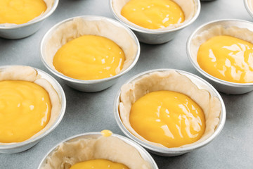 Small individual moulds with dough and cream ready to bake the typical Portuguese Belem cakes. Homemade pastries. Traditional pastries.