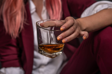 a glass of whiskey held by a girl in a burgundy suit with pink hair